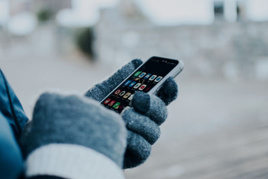 Close-up of hands using smartphone with gloves in winter, showing apps on screen.