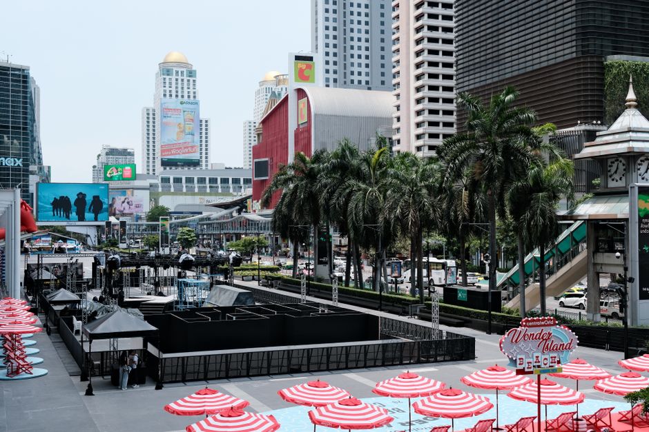 Lively urban scene in Bangkok with red umbrellas, modern buildings and palm trees in a bustling area.