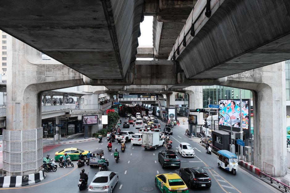 Busy urban street scene under elevated train tracks during the day.