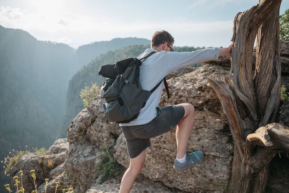 A man climbs rocky terrain with a backpack, showcasing adventure and nature exploration.