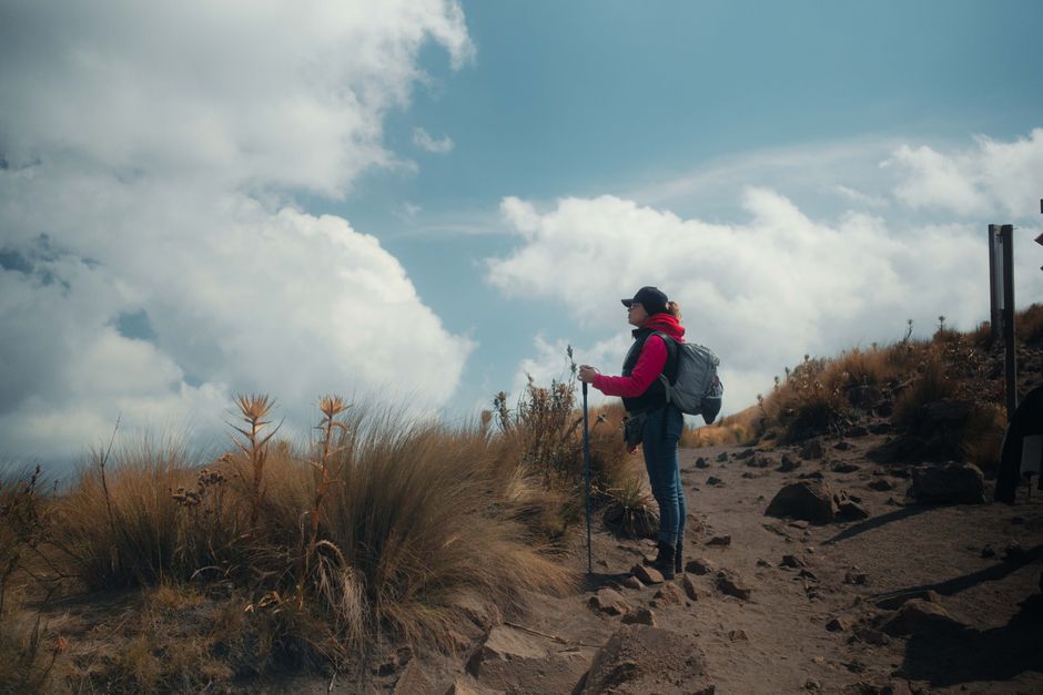 A female hiker explores a rugged mountain path under a vast blue sky.
