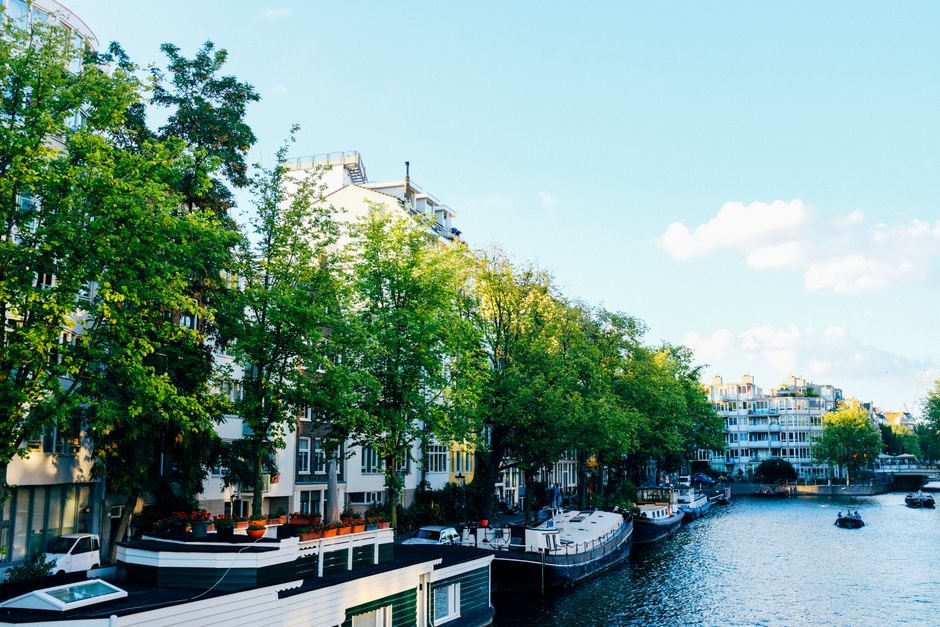 Perspective scenery of old city street with small residential houses located against calm canal with moored boats on clear spring day