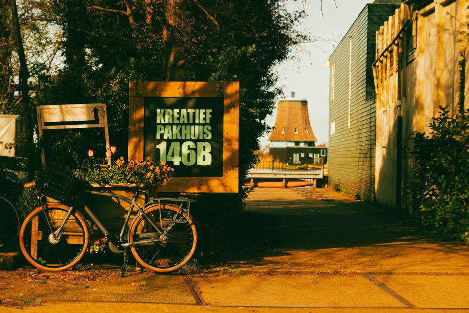 Bicycle parked near Kreatief Pakhuis 146B sign with windmill and sunny street in view.