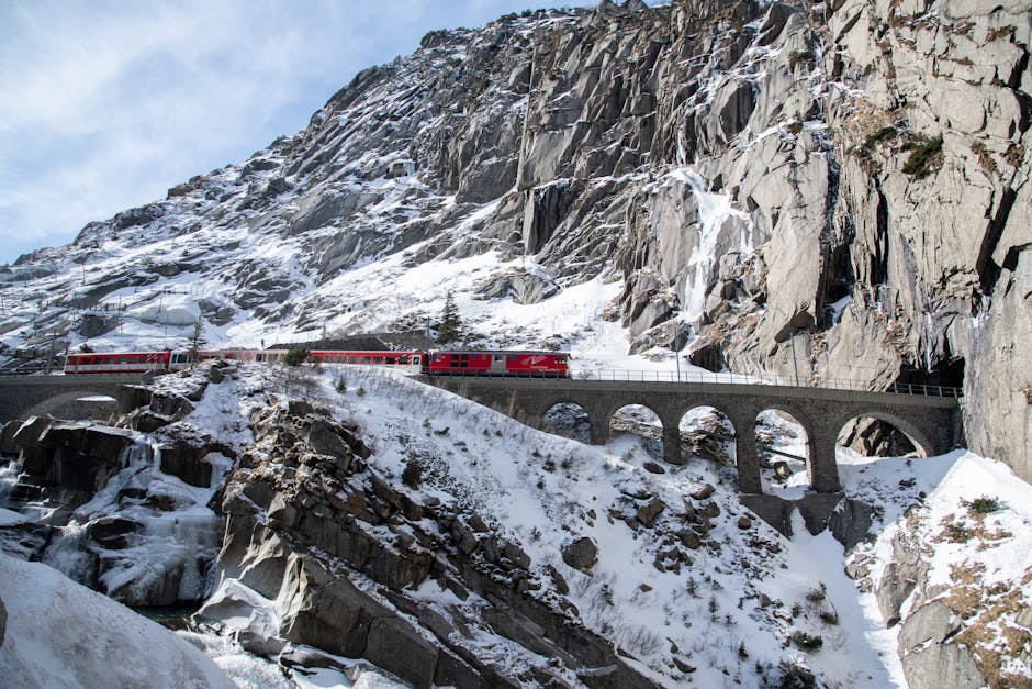 A vibrant red train traverses a scenic snowy viaduct in the Swiss Alps.