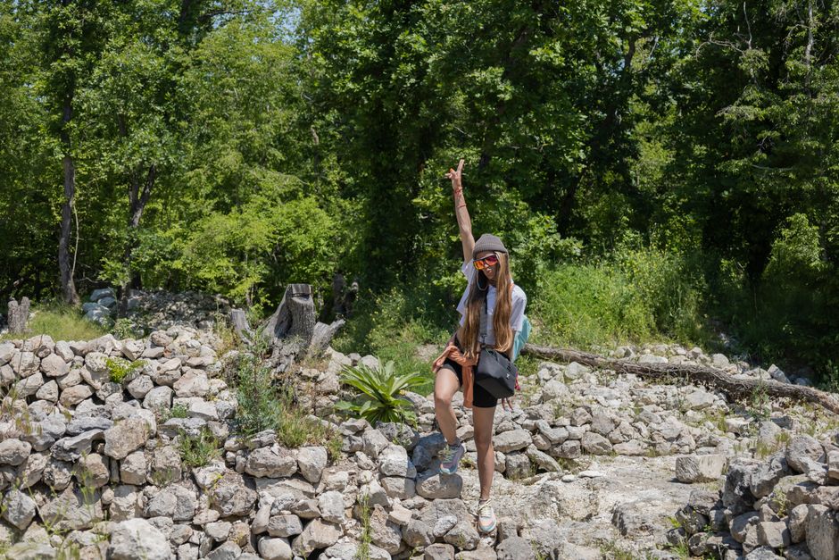 Woman posing in a rocky forest area with lush green trees, embodying adventure and exploration.