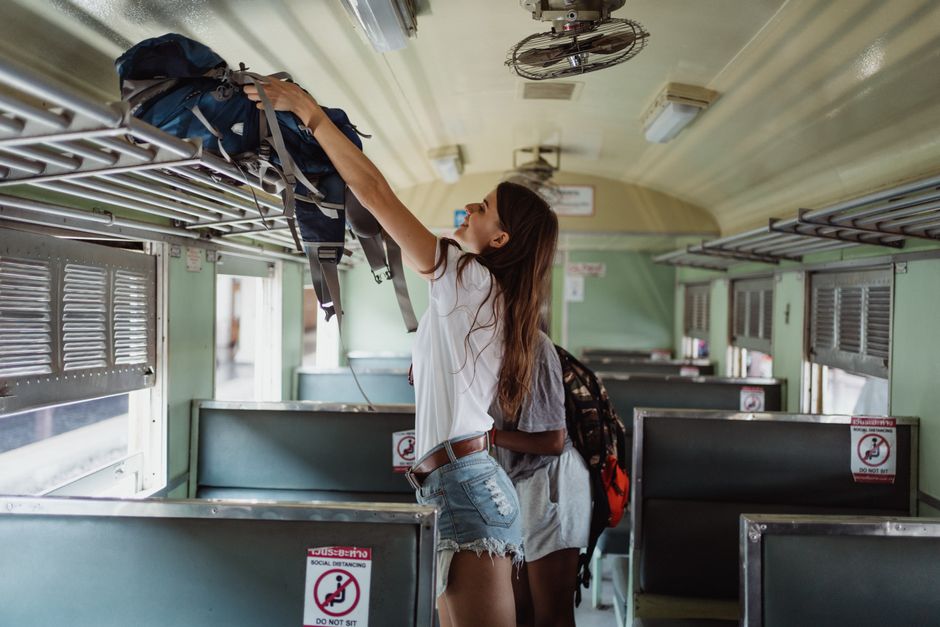 Woman placing backpack on luggage rack inside an empty train carriage.