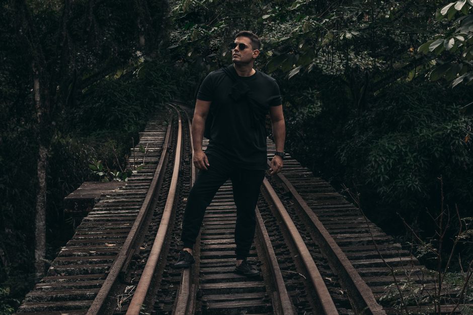 A man stands confidently on an overgrown railway, surrounded by dense Brazilian jungle.