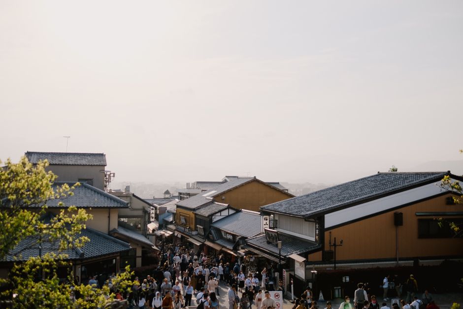 A lively street filled with people and traditional Japanese architecture under a hazy sky.