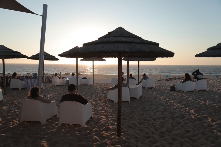 Beachgoers enjoying a serene sunset by the ocean in Lisbon, Portugal.