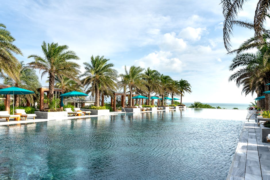 Relaxing scene of a luxury resort pool lined with palm trees and ocean view under a clear sky.