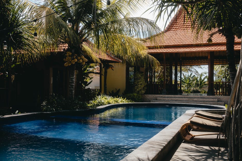 Relax by a luxurious tropical pool surrounded by lush palm trees under a sunny sky, perfect for summer getaways.