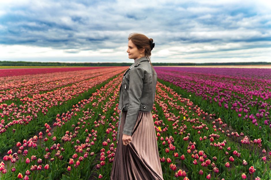 A woman in a field of vibrant tulips under a dramatic cloudy sky, capturing spring's beauty.