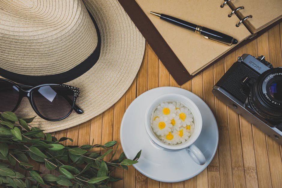 Flat lay of travel essentials with camera, hat, and tea cup.