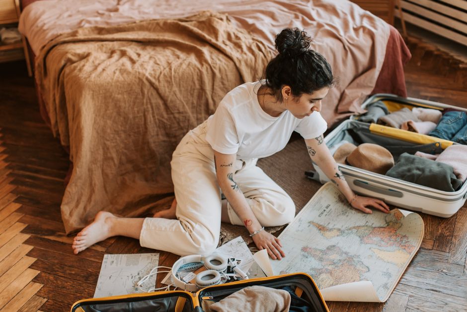 Young woman planning a travel route indoors, surrounded by luggage and a map.