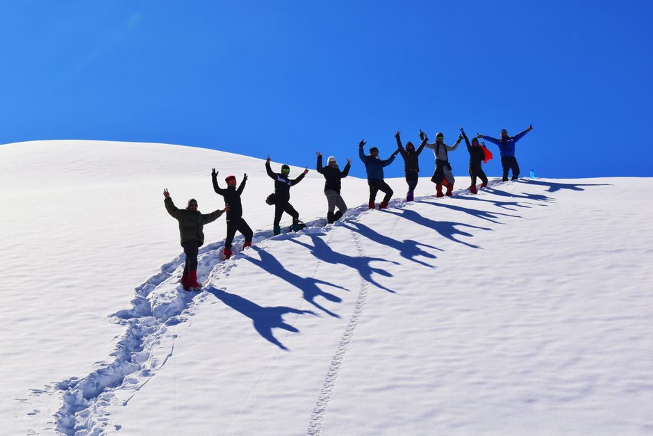 People enjoying a sunny hike on a snow-covered mountain with clear blue skies.
