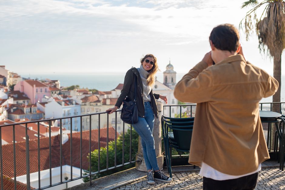 A couple taking photos with a beautiful view of Lisbon's architecture and the sea.