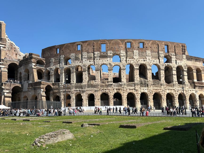 Historic Colosseum in Rome on a sunny day, bustling with visitors and vibrant atmosphere.