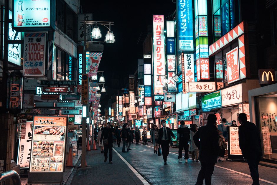 Explore the lively cityscape of Tokyo's streets illuminated by vibrant signage and energetic crowds at night.