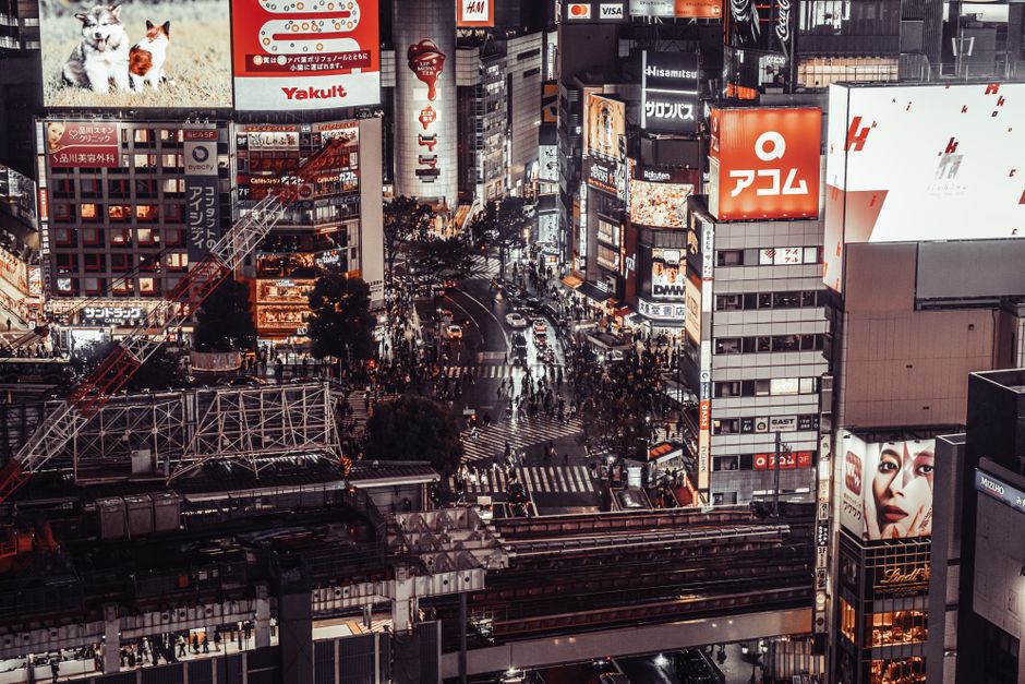 A bustling aerial view of Shibuya Crossing, Tokyo at night, showcasing vibrant city life and illuminated billboards.
