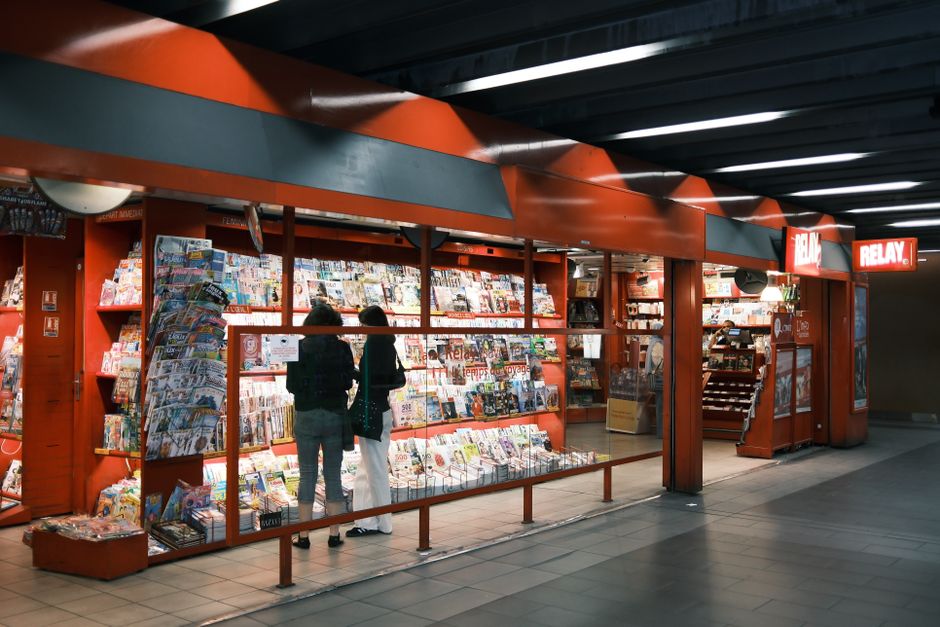Two adults browsing a newsstand stocked with magazines and newspapers in a modern indoor setting.