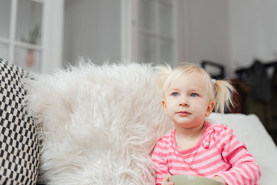 Adorable toddler in striped pink sweater sitting on a cozy sofa indoors.