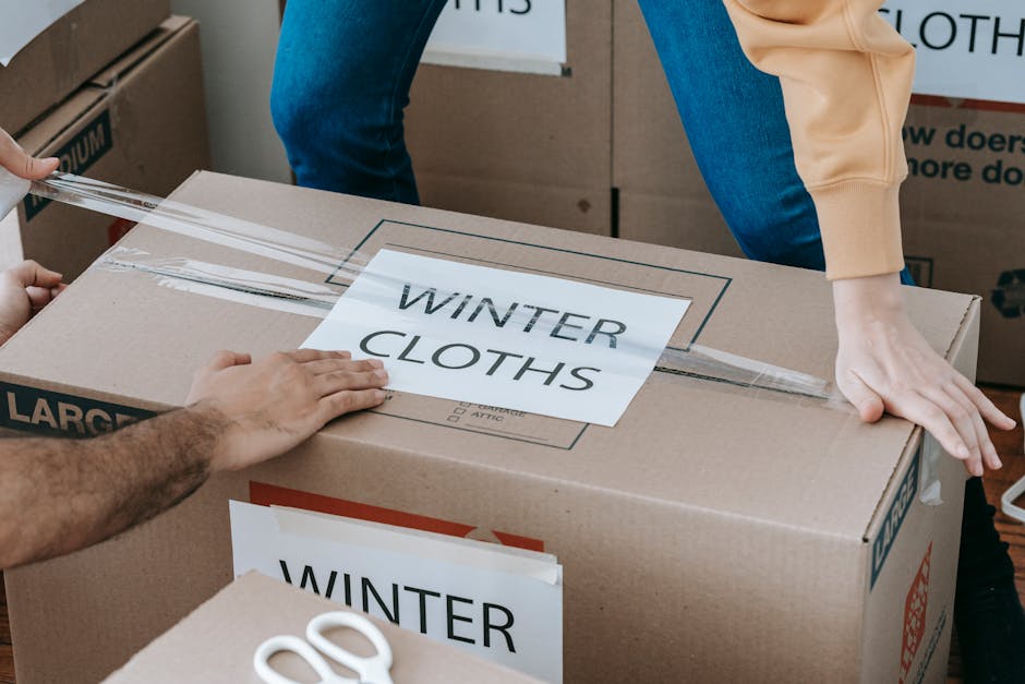 Close-up of hands packing a box labeled 'Winter Clothes' for relocation, emphasizing organized moving.