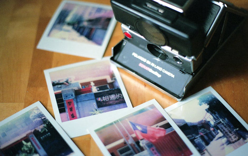A retro instant camera surrounded by colorful Polaroid photos on a wooden table.